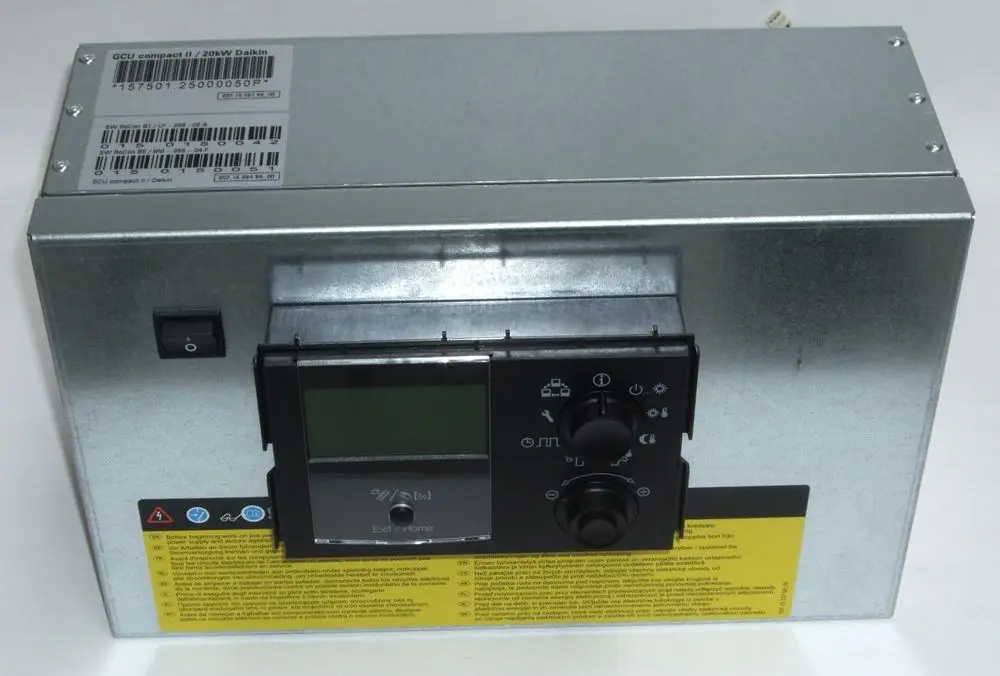 Daikin Steuergerät in metallischem Gehäuse mit Display, Bedienelementen und Warnhinweisen._links befindet sich ein Schalter. Gekennzeichnete Oberfläche mit Sicherheitsinformationen.